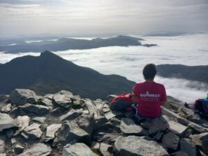 A spectacular shot of Kate with her back to the camera from Snowdon from above the clouds, after completing her 3 Peaks Challenge.