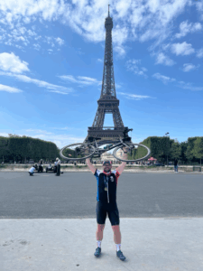 A triumphant Austin raising his bike in front of the Eiffel Tower after completing the London to Paris Bike Ride Cycle