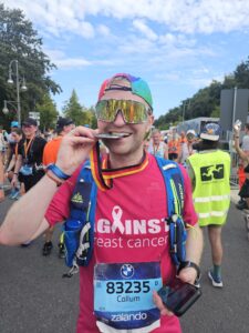 Callum in a pink ABC t-shirt biting his medal