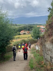 Several walkers with their backs down to the camera, walking into the distant Spanish countryside with mountains on the horizon.