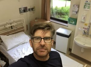 A selfie of Phil standing over a hospital bed.