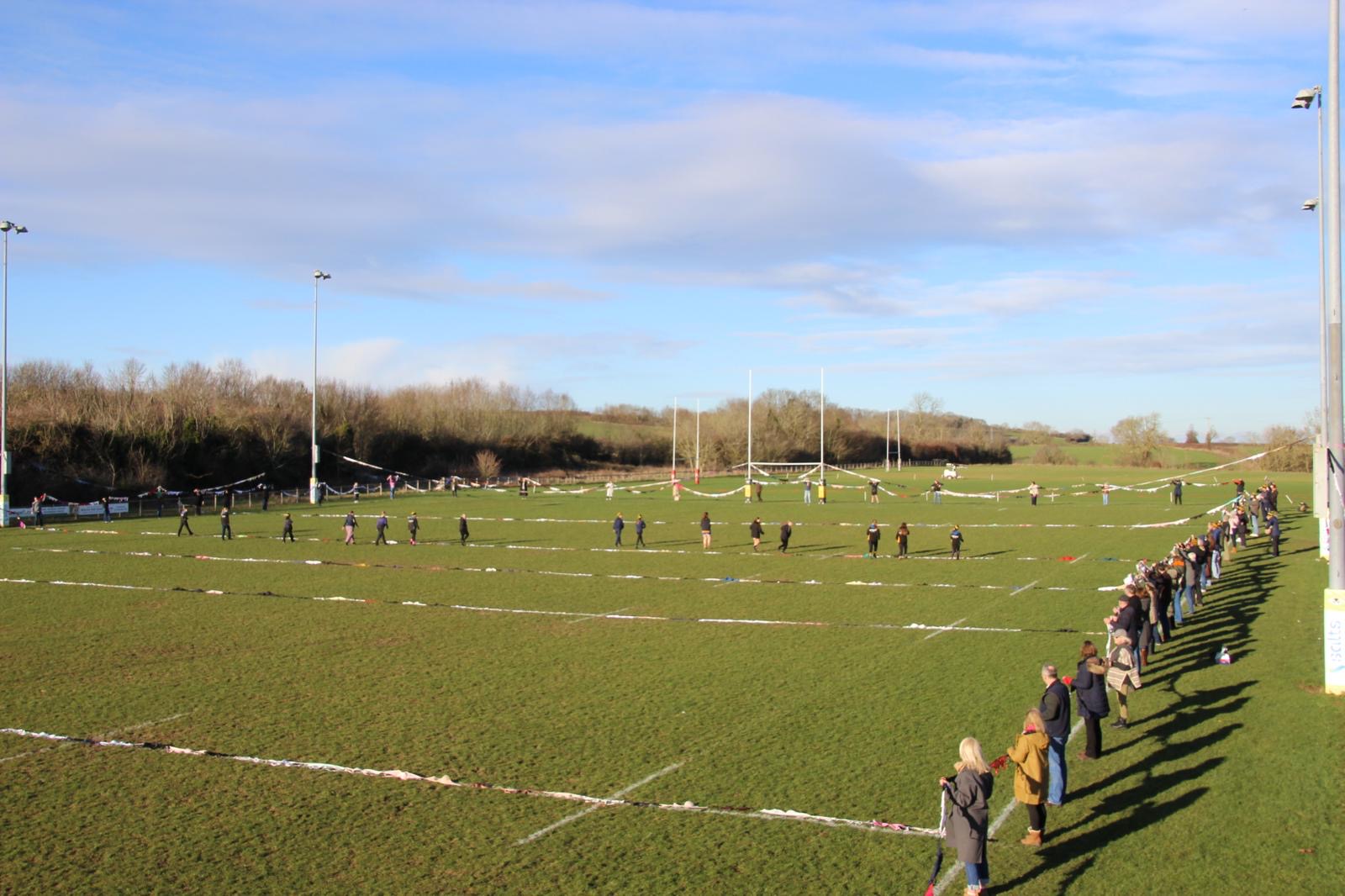 The pitch at Shipston-on-Stour Rugby Club with bras along the markings and people holding them up around the perimeter.