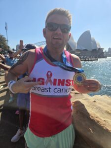 Justin pointing at this medal. Sydney Opera House is in the background