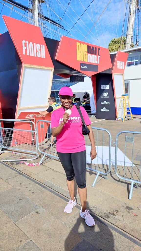 Peace, in a pink cap and Against Breast Cancer t-shirt, with her medal in front of the finishing line at Cutty Sark.