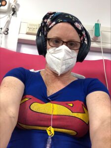 Rebecca in chemo, wearing a head covering, headphones and a face mask.